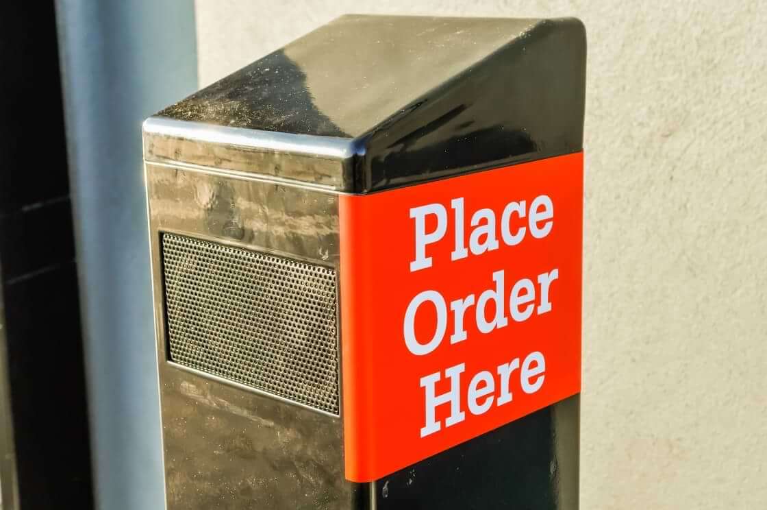 A black drive-through speaker with the words "Place Order Here" on the side in a white font on a red background. © By Stephen/stock.adobe.com. AI chatbots could soon be taking over drive-through orders at fast food restaurants across the US.