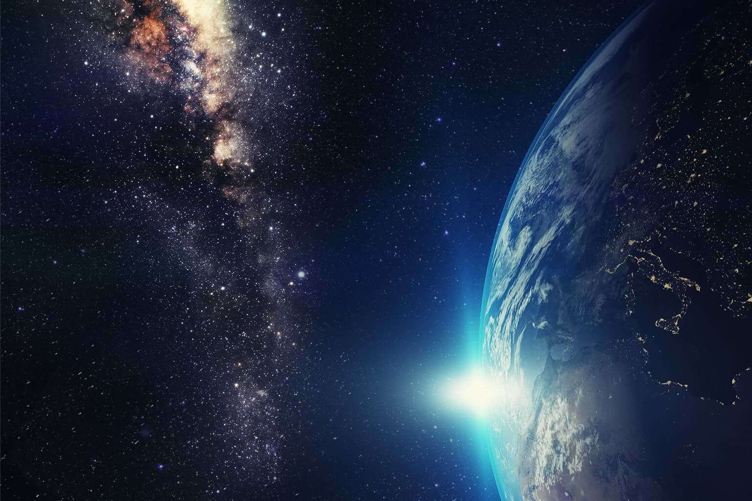In space, the sun peeks out from behind half of the earth on the right with a galaxy of stars seen to the left. © By janez volmajer