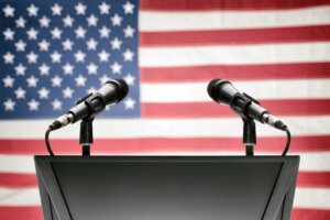 An empty podium with mics on both sides stands in front of an American flag, illustrating the recent presidential debates. © By niyazz/stock.adobe.com