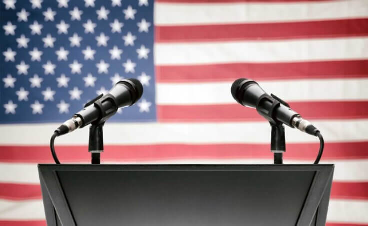 An empty podium with mics on both sides stands in front of an American flag, illustrating the recent presidential debates. © By niyazz/stock.adobe.com