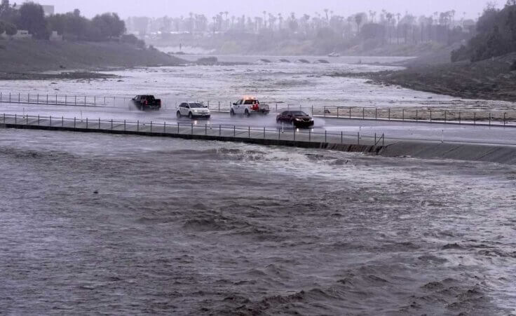 Vehicles cross over a flood control basin that has almost reached the street, Sunday, Aug. 20, 2023, in Palm Desert, Calif. Forecasters said Tropical Storm Hilary was the first tropical storm to hit Southern California in 84 years, bringing the potential for flash floods, mudslides, isolated tornadoes, high winds and power outages. (AP Photo/Mark J. Terrill)