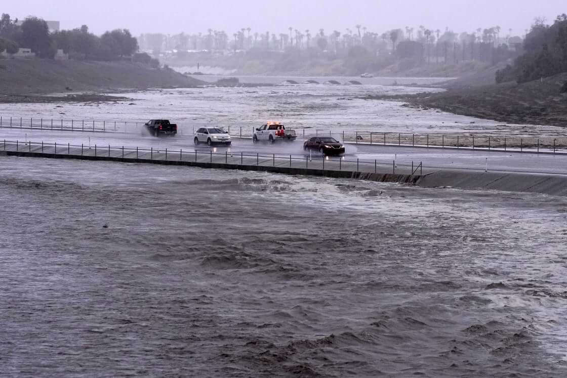 Vehicles cross over a flood control basin that has almost reached the street, Sunday, Aug. 20, 2023, in Palm Desert, Calif. Forecasters said Tropical Storm Hilary was the first tropical storm to hit Southern California in 84 years, bringing the potential for flash floods, mudslides, isolated tornadoes, high winds and power outages. (AP Photo/Mark J. Terrill)
