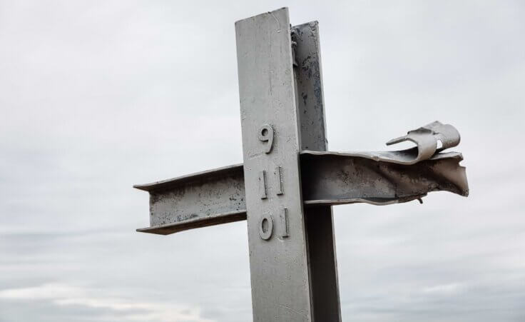 Two beams from the 9/11 attacks on the World Trade Towers form a cross. The numbers 9-11-01 are stamped on the center beam. misu /stock.adobe.com