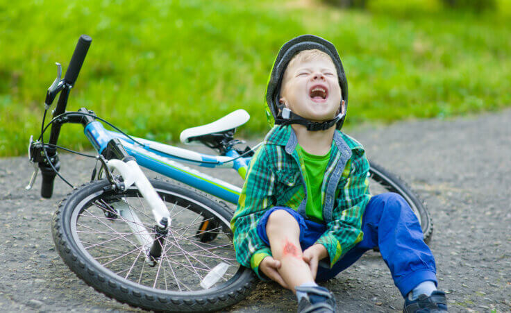 A child sits next to his fallen bike, grabbing at his scraped knee, a depiction of innocent suffering. Ermolaev Alexandr/stock.adobe.com