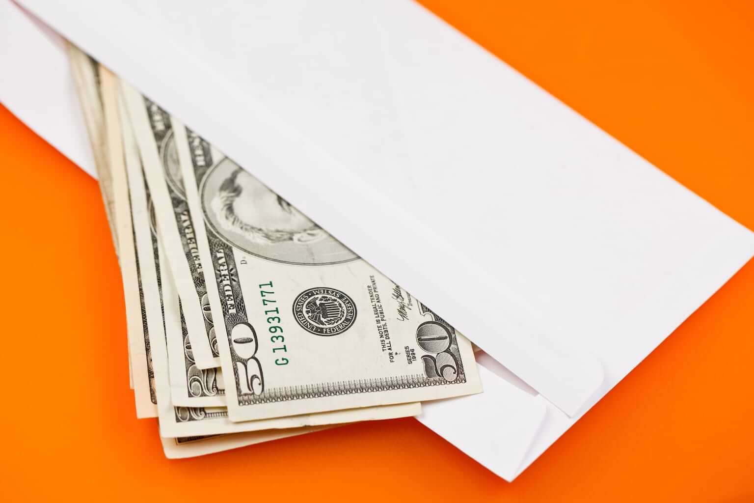Money spills out of an open white envelope against an orange background. By Jiri Hera/stock.adobe.com