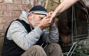 A homeless man grasps the outstretched arm of a woman, an illustration of the Micah Mandate from Micah 6:8. By stephm2506/stock.adobe.com