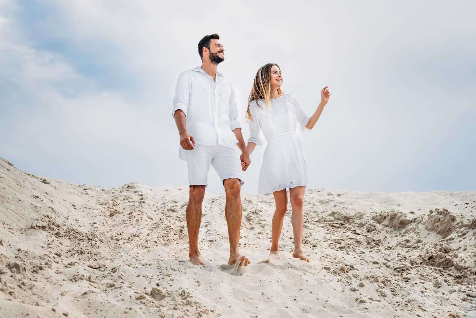A man and woman, both dressed in white summer clothes, hold hands as they walk barefoot on a sandy dune. By LIGHTFIELD STUDIOS/stock.adobe.com. An illustration of the origin of why you can't white after Labor Day