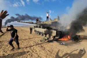 Palestinians celebrate by a destroyed Israeli tank at the Gaza Strip fence east of Khan Younis southern Saturday, Oct. 7, 2023. (AP Photo/Hassan Eslaiah). How did the war in Israel start?
