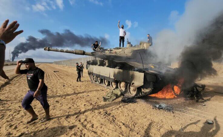 Palestinians celebrate by a destroyed Israeli tank at the Gaza Strip fence east of Khan Younis southern Saturday, Oct. 7, 2023. (AP Photo/Hassan Eslaiah). How did the war in Israel start?
