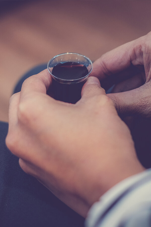A woman holds a small plastic cup filled with red communion wine. By Win/stock.adobe.com