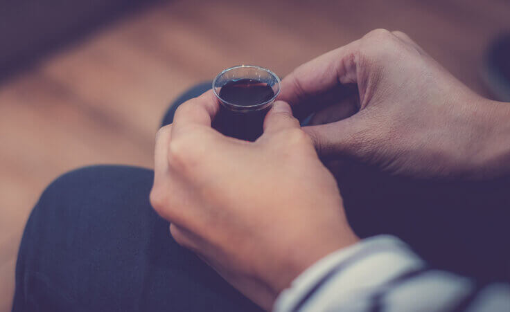 A woman holds a small plastic cup filled with red communion wine. By Win/stock.adobe.com