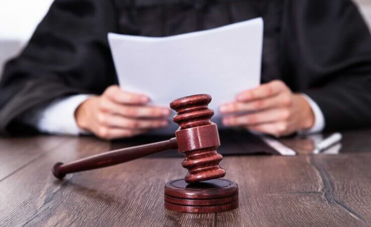 A gavel rests horizontally in front of a judge holding papers. By Andrey Popov/stock.adobe.com