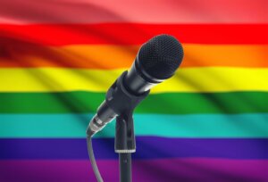 A microphone on a stand in front of a rainbow LGBTQ flag. By niyazz/stock.adobe.com