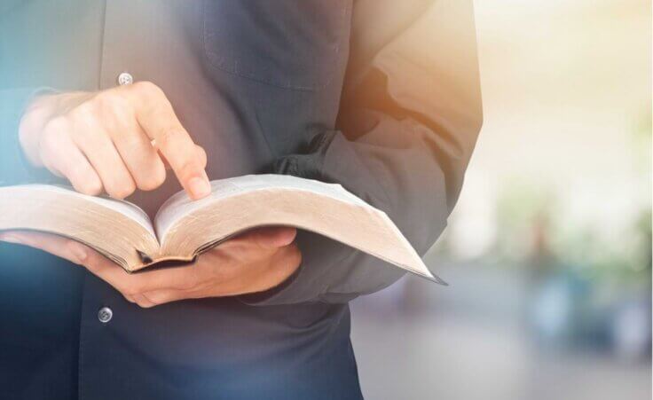 A man holds an open Bible in his hands, pointing to a verse with his right index finger. BillionPhotos.com/stock.adobe.com