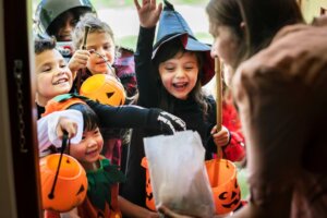 A group of children in Halloween costumes reach into a bag of candy while trick-or-treating. By Rawpixel.com/stock.adobe.com. Why is Halloween so popular?