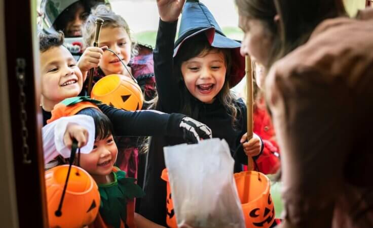 A group of children in Halloween costumes reach into a bag of candy while trick-or-treating. By Rawpixel.com/stock.adobe.com. Why is Halloween so popular?