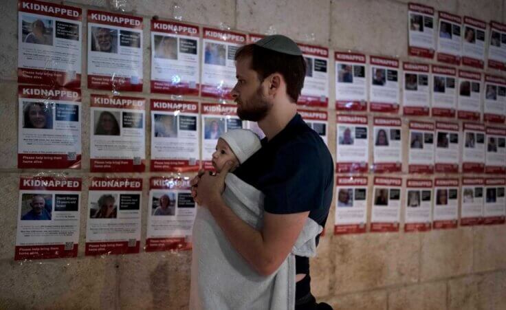FILE - A man holds his baby as he looks at posters of the men, women and children held hostage by Hamas in the Gaza Strip, during a vigil marking 30 days since the Oct. 7 Hamas attack that started the fighting, in Jerusalem, Israel on Nov. 5, 2023. (AP Photo/Maya Alleruzzo, File)