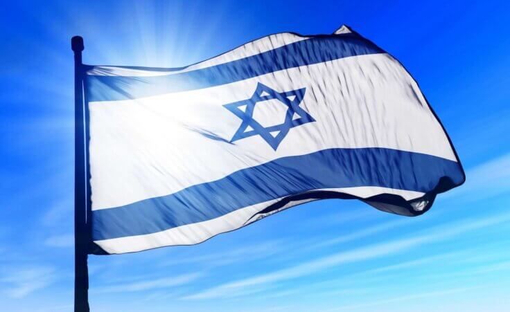 The sun shines through a waving flag of Israel. By Lulla/stock.adobe.com