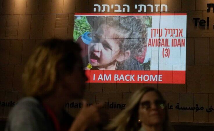 People walk past an image of 4-year-old Abigail Edan, a hostage held by Hamas who was released on Sunday, projected onto a building in Tel Aviv, Sunday, Nov 26, 2023. (AP Photo/Ariel Schalit)
