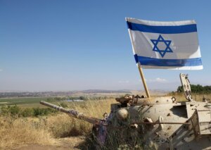 An Israeli tank sits in a field with an Israel flag upright within the tank. By Maurizio/stock.adobe.com