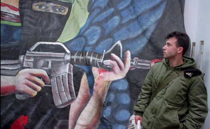 FILE - An Israeli soldier stands next to a Hamas propaganda poster seized during recent raids, at an Israeli army base in Hebron, March 7, 1996. (AP Photo/ Jacqueline Arzt, File)