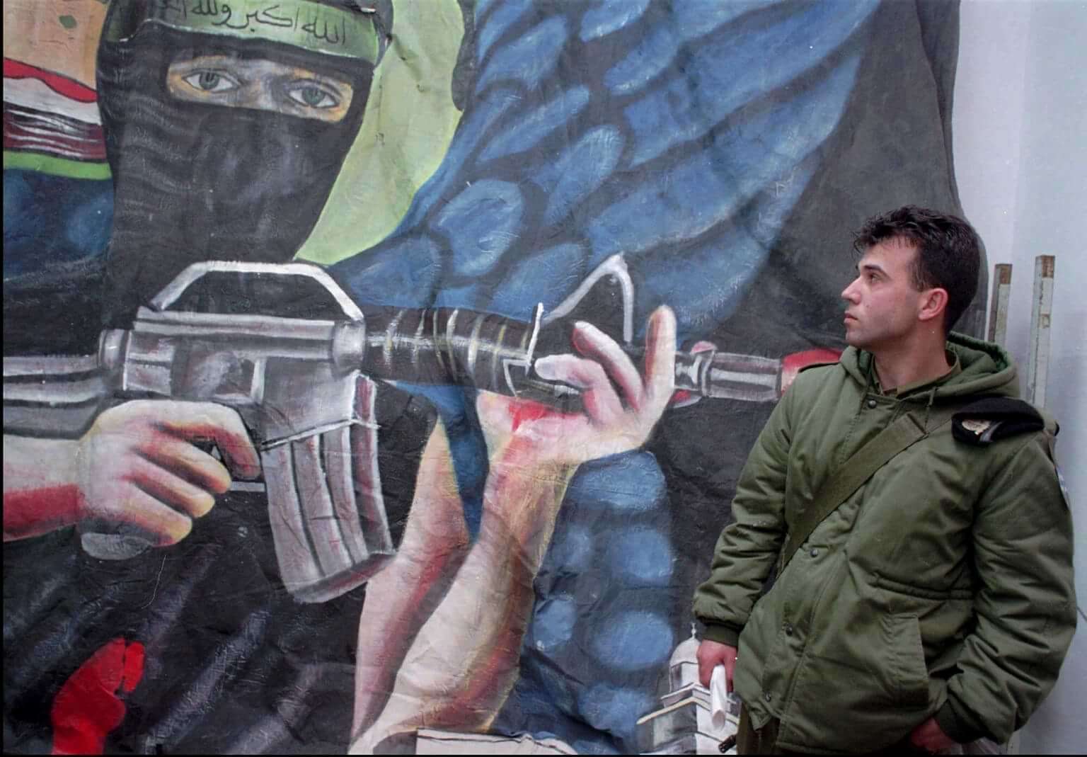 FILE - An Israeli soldier stands next to a Hamas propaganda poster seized during recent raids, at an Israeli army base in Hebron, March 7, 1996. (AP Photo/ Jacqueline Arzt, File)