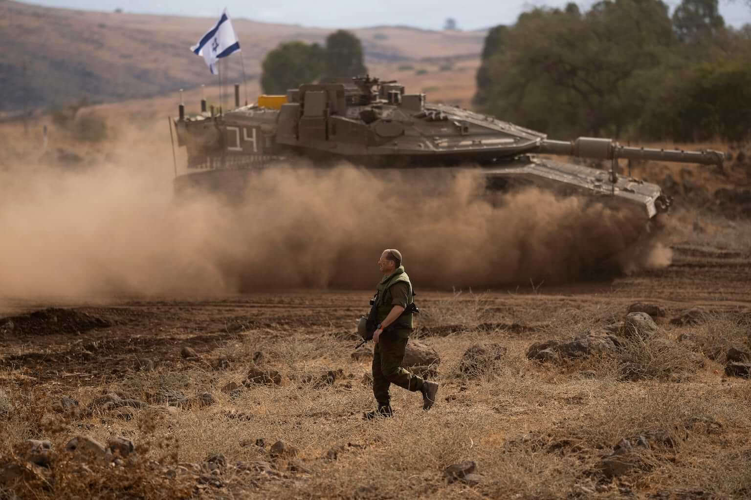 An Israeli soldier walks in front of a moving tank with an Israeli flag on the top in a staging area near the Israeli border with Lebanon, on Sunday, Oct. 15, 2023. (AP Photo/Petros Giannakouris) How should Israel respond to Hamas?
