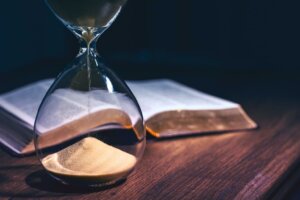 An hourglass that's almost out of time stands in front of an open Bible on a desk. By JavierArtPhotography/stock.adobe.com. Are we living in the last days?