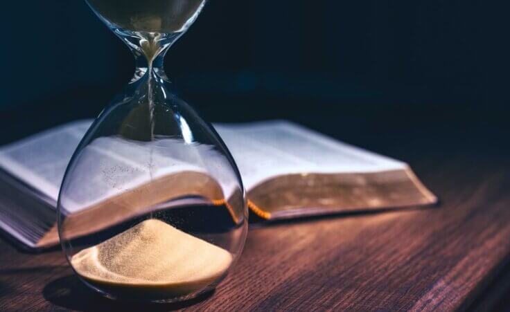 An hourglass that's almost out of time stands in front of an open Bible on a desk. By JavierArtPhotography/stock.adobe.com. Are we living in the last days?