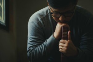 A man in glasses bows his head in prayer while holding a Bible upright on a table, its spine and the word "BIBLE" facing out. By Pcess609/stock.adobe.com. Many pastors and church leaders suffer from compassion fatigue.