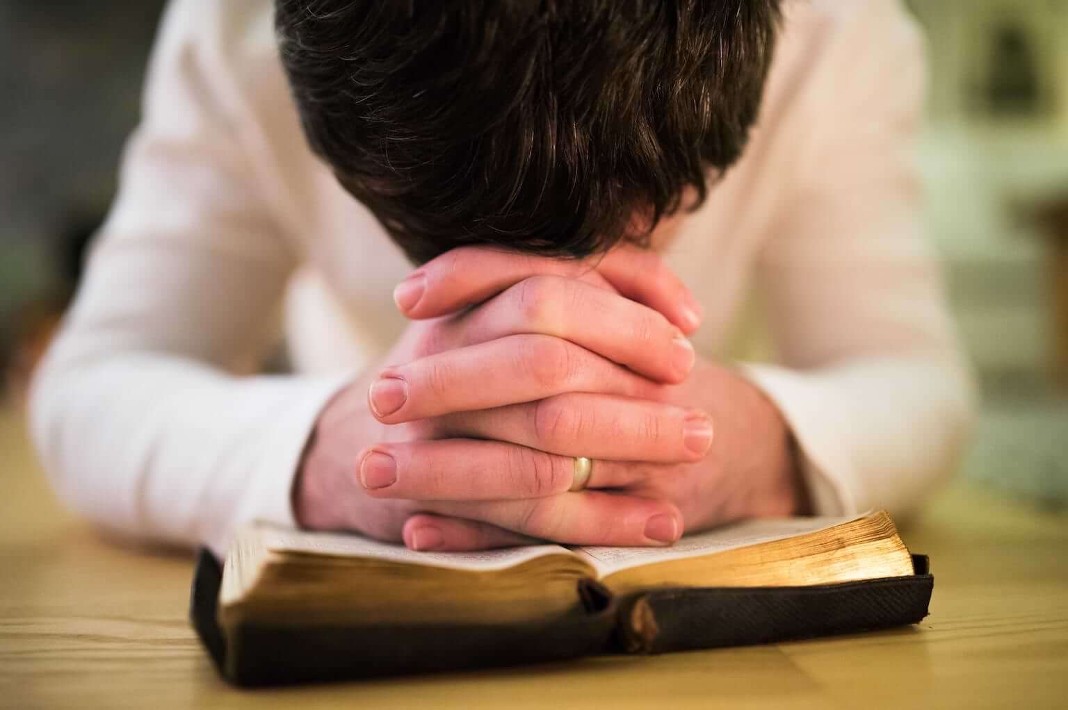A man bows his hand on top of his clasped hands in prayer, which are resting on an open Bible. By Halfpoint/stock.adobe.com. The war in Israel is an urgent call for Christians to engage in spiritual warfare.