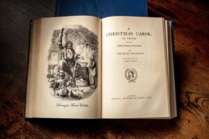 Charles Dickens' book "A Christmas Carol" lies open featuring an illustration of "Scrooge's Third Vistor" on the left page and the title page on the right. By laplateresca/stock.adobe.com