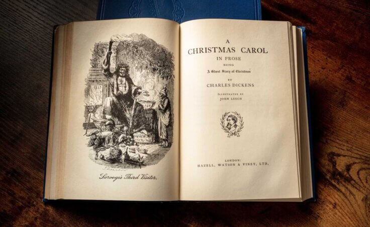 Charles Dickens' book "A Christmas Carol" lies open featuring an illustration of "Scrooge's Third Vistor" on the left page and the title page on the right. By laplateresca/stock.adobe.com