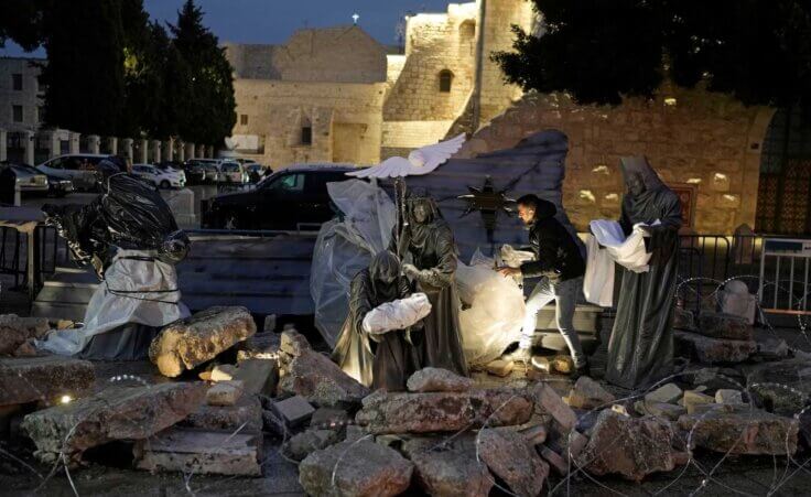 A man decorates a nativity scene with rubble around symbolizing the destruction in Gaza and white sheets referring to the dead civilians, in Manger Square, adjacent to the Church of the Nativity, in Bethlehem, Friday, Dec. 23, 2023. Bethlehem is having a subdued Christmas after officials in Jesus' traditional birthplace decided to forgo celebrations due to the Israel-Hamas war.(AP Photo/Leo Correa)