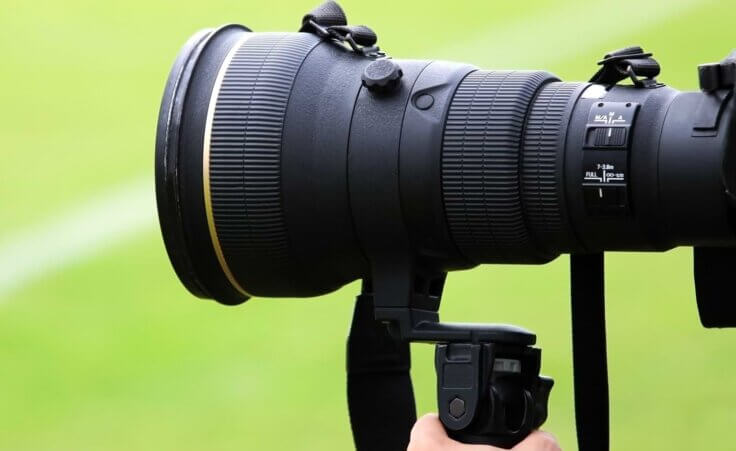 A photorapher's hand holds a telephoto lens at a sporting event. By TopMicrobialStock/stock.adobe.com. Nash Pils is becoming an increasingly well-known sports photographer.