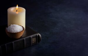 A lit candle and a handful of salt in a small bowl sit atop a black Bible. By pamela_d_mcadams/stock.adobe.com