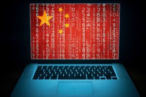 An open laptop's screen shows lines of code superimposed over China's flag, an illustration of China's increasing cybersecurity attacks on America. By littlewolf1989/stock.adobe.com.