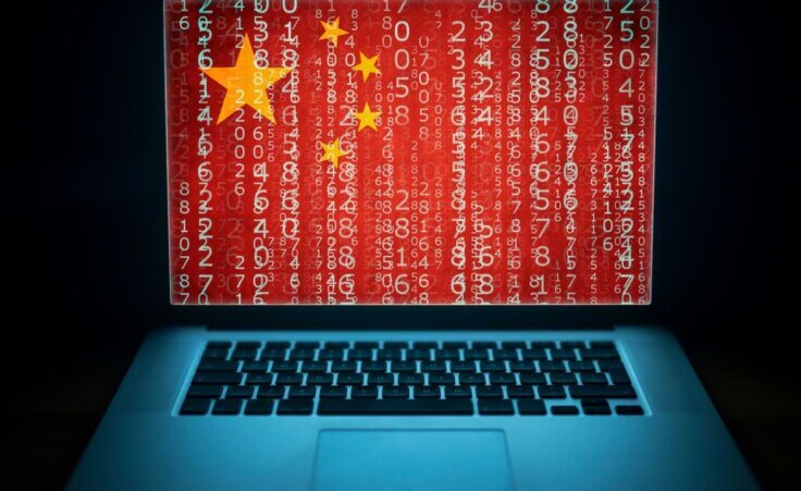 An open laptop's screen shows lines of code superimposed over China's flag, an illustration of China's increasing cybersecurity attacks on America. By littlewolf1989/stock.adobe.com.