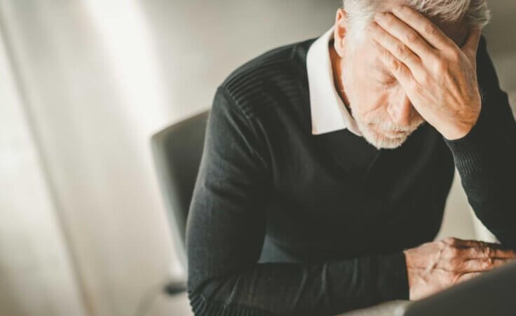 A gray-haired man holds his left hand to his forehead in a sign of frustration, an illustration of the growing problem of clergy burnout. By thodonal/stock.adobe.com