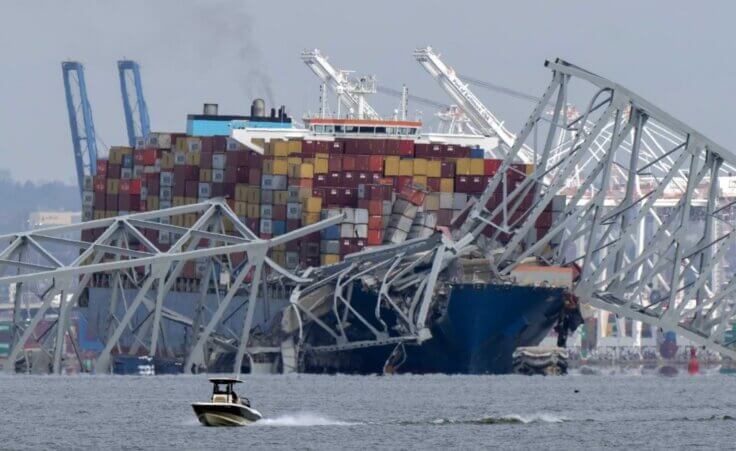 A boat moves past a container ship as it rests against wreckage of the Francis Scott Key Bridge on Tuesday, March 26, 2024, as seen from Pasadena, Md. (AP Photo/Mark Schiefelbein). The bridge disaster in Baltimore has resulted in at least 6 dead.