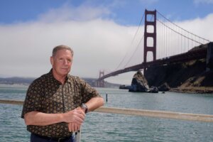 In this Aug. 3, 2021 photo retired California Highway Patrol officer Kevin Briggs poses below the Golden Gate Bridge near Sausalito, Calif. Briggs responded to many suicide attempts on the Golden Gate Bridge during his career. He met Kevin Berthia in 2005 when Berthia attempted suicide and now the two speak nationally about suicide prevention. Briggs joined the CHP in 1990 and began responding to emergencies on the bridge in 1994, where he would work with people in crisis four to six times a month. He retired in 2013. (AP Photo/Eric Risberg)