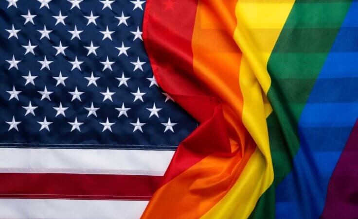 An LGBTQ+ rainbow flag overlaps an American flag. By nevodka.com/stock.adobe.com