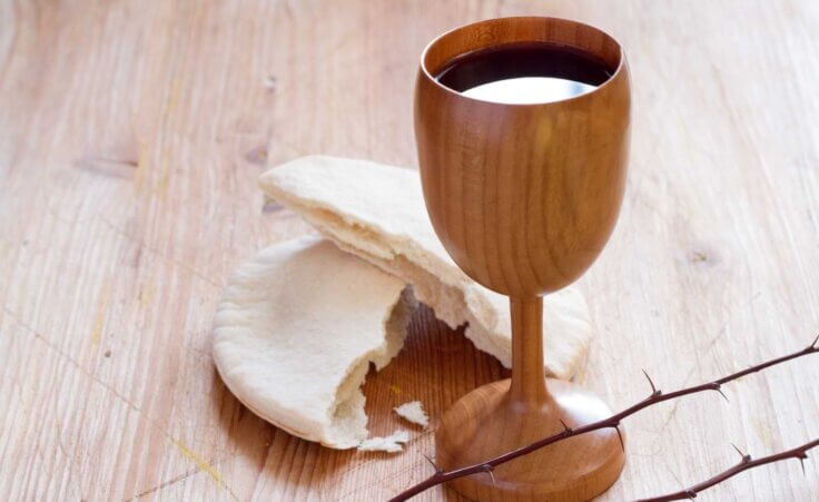 Symbolizing the Passover meal that Jesus took at the Last Supper, a chalice filled with wine and Passover bread sits atop a table. By udra11/stock.adobe.com.