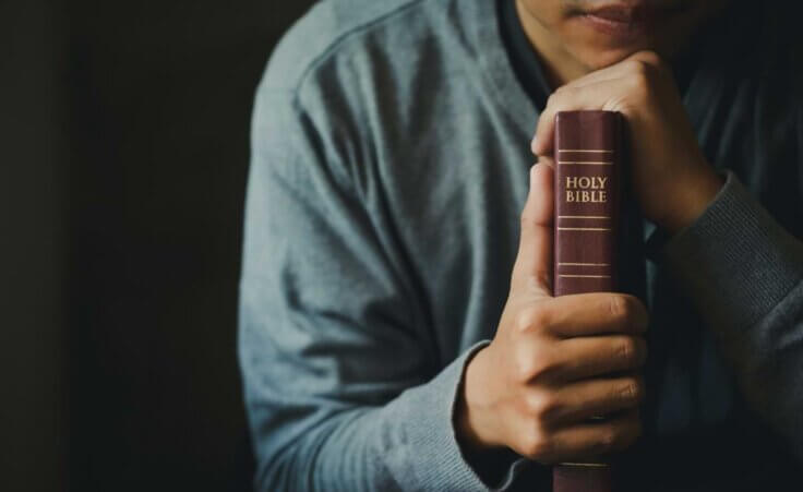 A man clutches a Bible in front him, its spine out featuring the words HOLY BIBLE. By Pcess609/stock.adobe.com