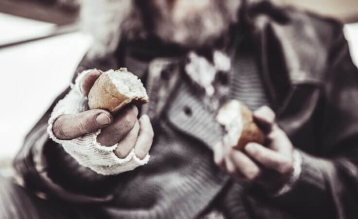 Homeless man holding out a piece of bread. By Viacheslav Yakobchuk/stock.adobe.com