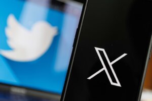 In the background, the Twitter bird logo appears on a computer monitor. In the foreground, the X logo is seen on a black phone screen. By Rokas/stock.adobe.com
