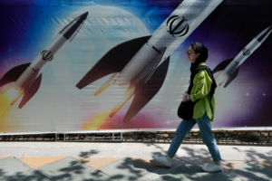 A woman walks past a banner showing missiles being launched, in northern Tehran, Iran, Friday, April 19, 2024. Iran fired air defenses at a major air base and a nuclear site near the central city of Isfahan after spotting drones early Friday morning, raising fears of a possible Israeli strike in retaliation for Tehran's unprecedented drone-and-missile assault on the country. On the missiles, a decorative sign reads: "Allah" (AP Photo/Vahid Salemi)