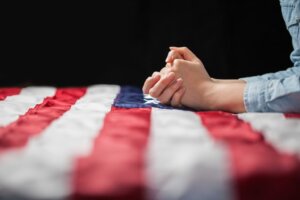 Clasped hands in prayer on top of an American flag. By 4Max/stock.adobe.com