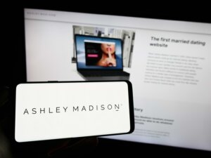 Person holding cellphone with logo of online dating company The Ashley Madison Agency on screen in front of webpage. By Timon/stock.adobe.com