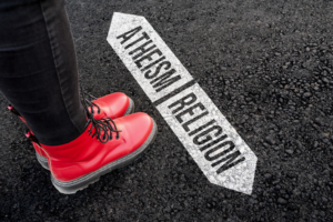 Woman with boots is standing on asphalt next to arrow signs of words atheism and religion. By mirsad/stock.adobe.com. religious demographics